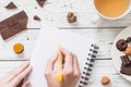 WomanÃ¢â¬â¢s hands writing in a blank notebook, cup of tea and raw vegan chocolate candies Royalty Free Stock Photo